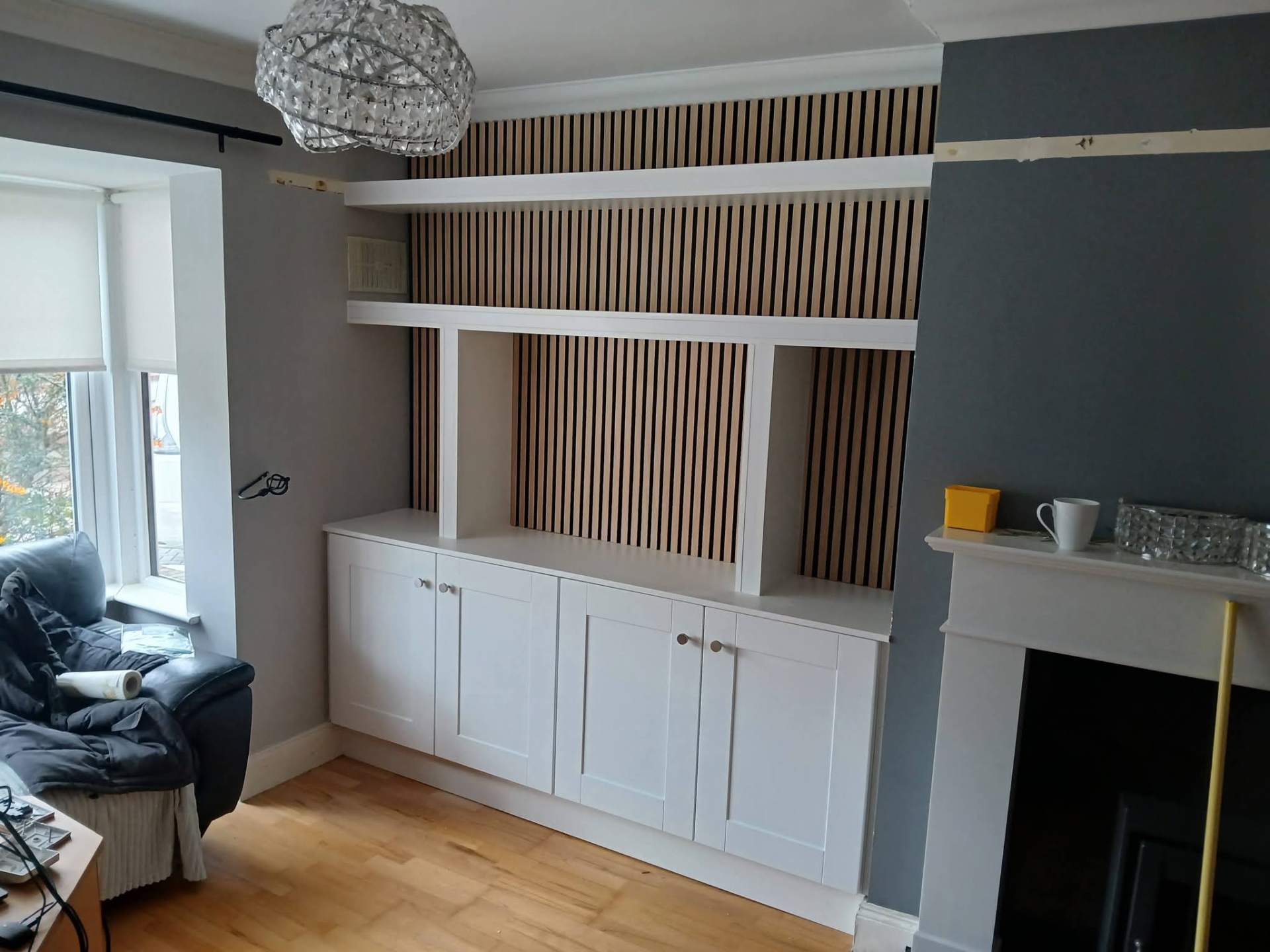 Built-in media wall with white shelving, oak slat feature panel and shaker base cabinets beside a fireplace