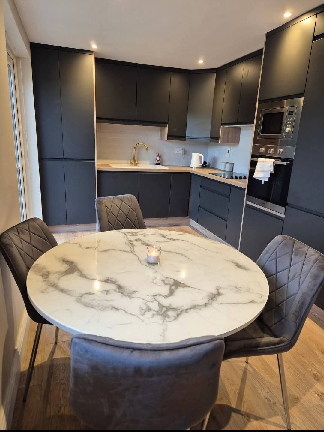 Handleless matte graphite kitchen with oak-effect worktop, brass tap and integrated ovens